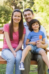 Fototapeta premium Smiling couple with son sitting on park bench