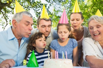 Extended family blowing cake outdoors