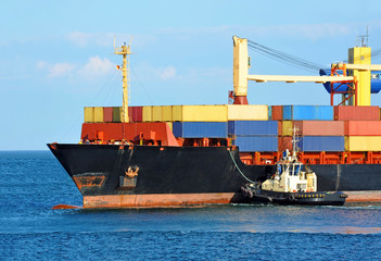 Tugboat assisting container cargo ship to harbor quayside
