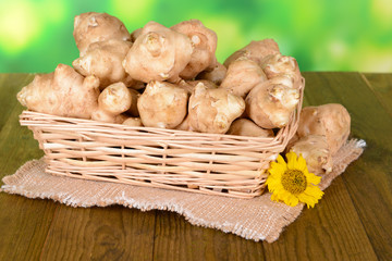 Topinambur roots in wicker basket on table on bright background
