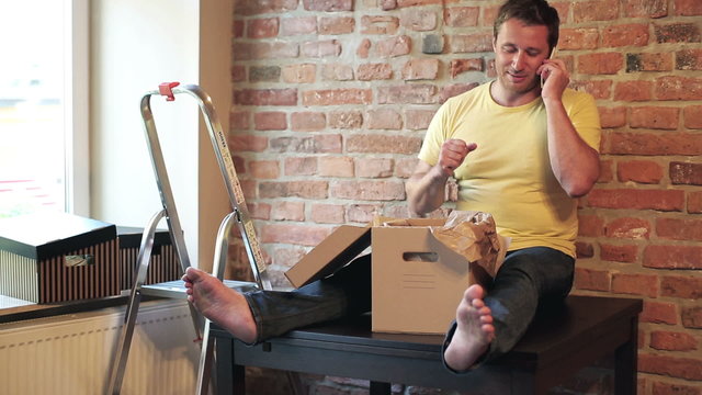 man sitting on the table in his new flat and talking on the phon