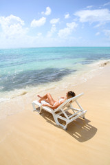 Fototapeta na wymiar Woman relaxing in long chair by the beach