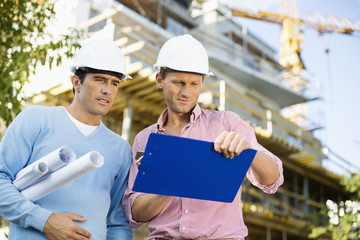 Male architects with blueprint and clipboard working at site