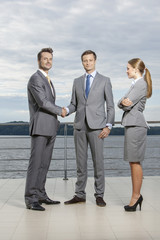 Full length portrait of young businessmen shaking hands while businesswoman looking at them on terrace