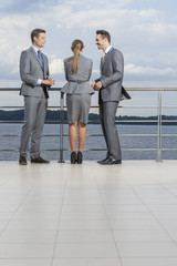 Young businesspeople standing at terrace railings against sky