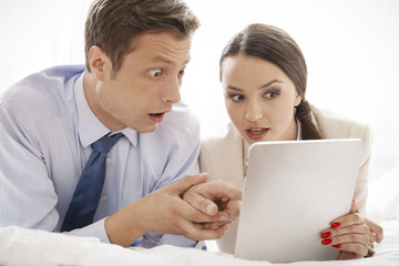 Shocked business couple using digital tablet in hotel