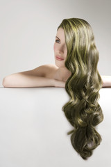 Thoughtful woman with long green dyed hair against gray background