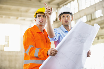 Male architects with blueprint working at construction site