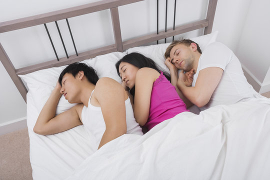 Young woman sleeping with two men in bed