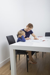 Mid adult man helping boy in studies at table