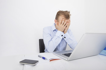 Tired businessman with hands on face sitting at desk by laptop