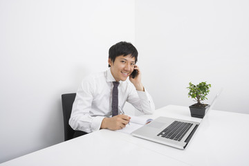 Portrait of happy businessman using cell phone while working at office desk