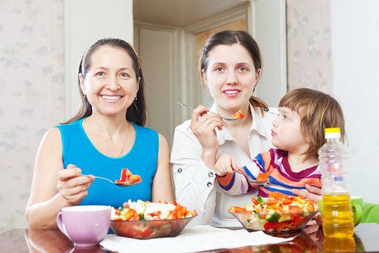 Mature woman and adult daughter with baby eats vegetables