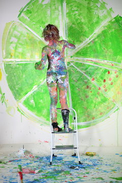 Naked girl covered in paint standing on ladder in studio