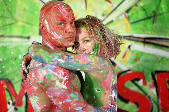 Naked girl hug bald man all in the paint in studio