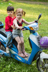 Korean boy and caucasian girl on a blue scooter on nature
