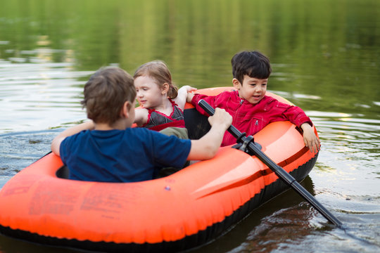Three little friends floating in a rubber boat on the pond