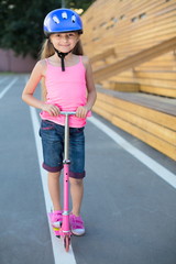 Little girl in helmet with scooter on running track on stadium