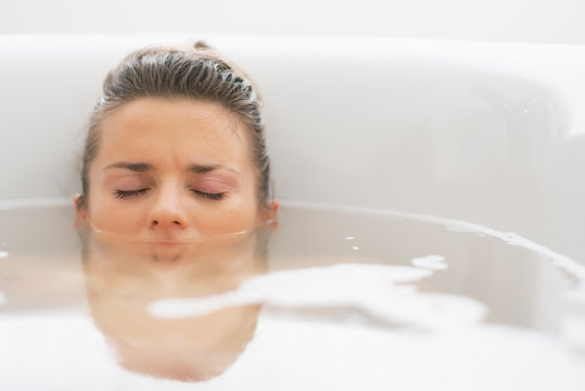 Stressed young woman laying under water in bathtub