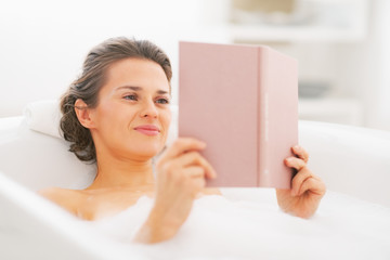 Happy young woman reading book in bathtub