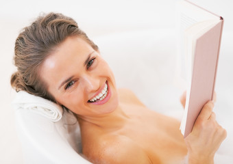 Obraz premium Smiling young woman reading book in bathtub