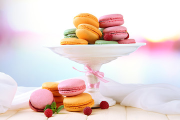 Gentle macaroons in vase on table on light background
