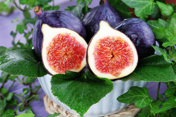 Ripe figs in bowl in leaves on wooden table close-up