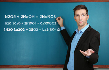 Young teacher near chalkboard in school classroom