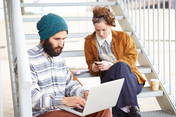 Hipster couple using computer and smartphone outdoors