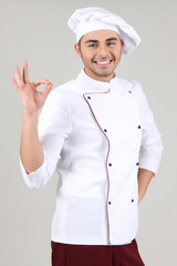 Professional chef in white uniform and hat, on gray background
