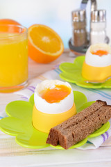 Boiled eggs in egg cups on table on light background