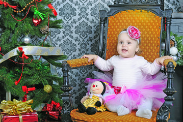 Small girl in easy chair near new year's fir tree