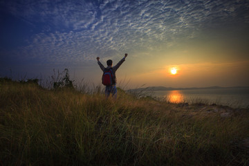 young man standing and rising hand as victory on grass hill