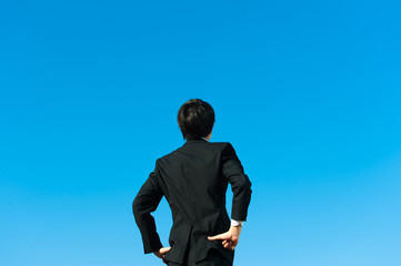 やる気を出す男性ビジネスマンの後ろ姿と青空