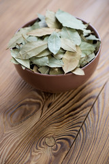 Bowl with dried bay leaves on a wooden table, vertical shot