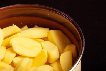 Raw peeled potatoes in pot pan on black. Healthy food.