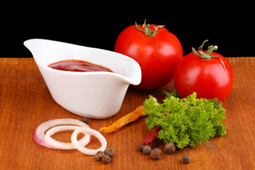 Ketchup and ripe tomatoes on wooden table on black background