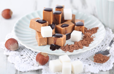 Many toffee on plate and cup of tea on napkin on wooden table
