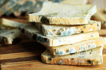 Mouldy bread on cutting board, on wooden background
