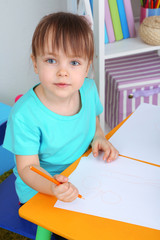 Little girl draws sitting at table in room