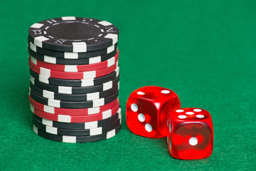 red and black poker chips and dice on a green casino felt