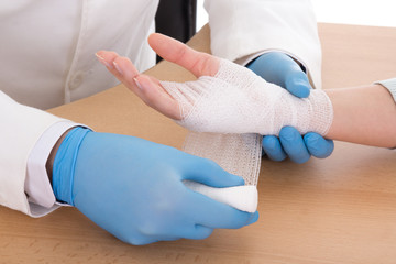 close up of young male doctor bandaging female hand