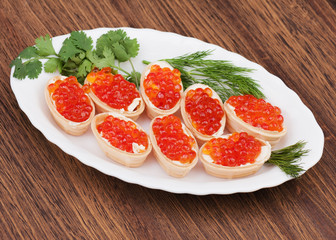 Tartlets with red caviar on wooden background.