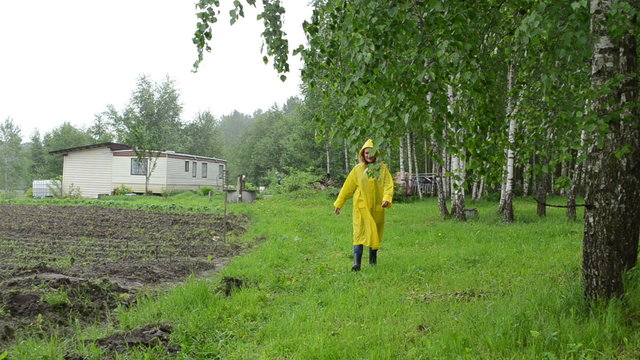 Woman in water proof coat near birch tree and small garden house