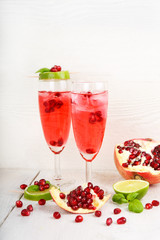 Two glasses with red pomgranate champagne, lime and mint.