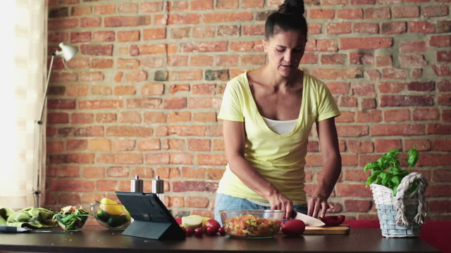 Young woman preparing salad and checking recipe on tablet comput