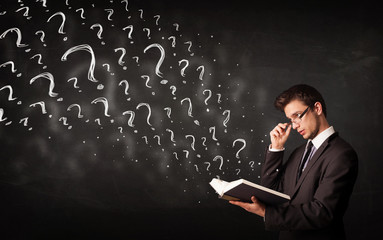 Young man reading a book with question marks coming out from it