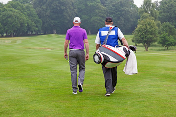 Golfer and caddy walking up a fairway - 59975581