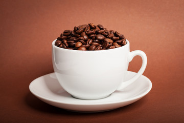 Coffee beans in cup on brown background