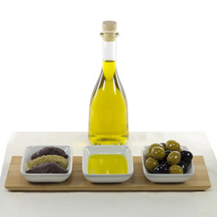 Olive oil in glass bottle and dished olive products over wooden